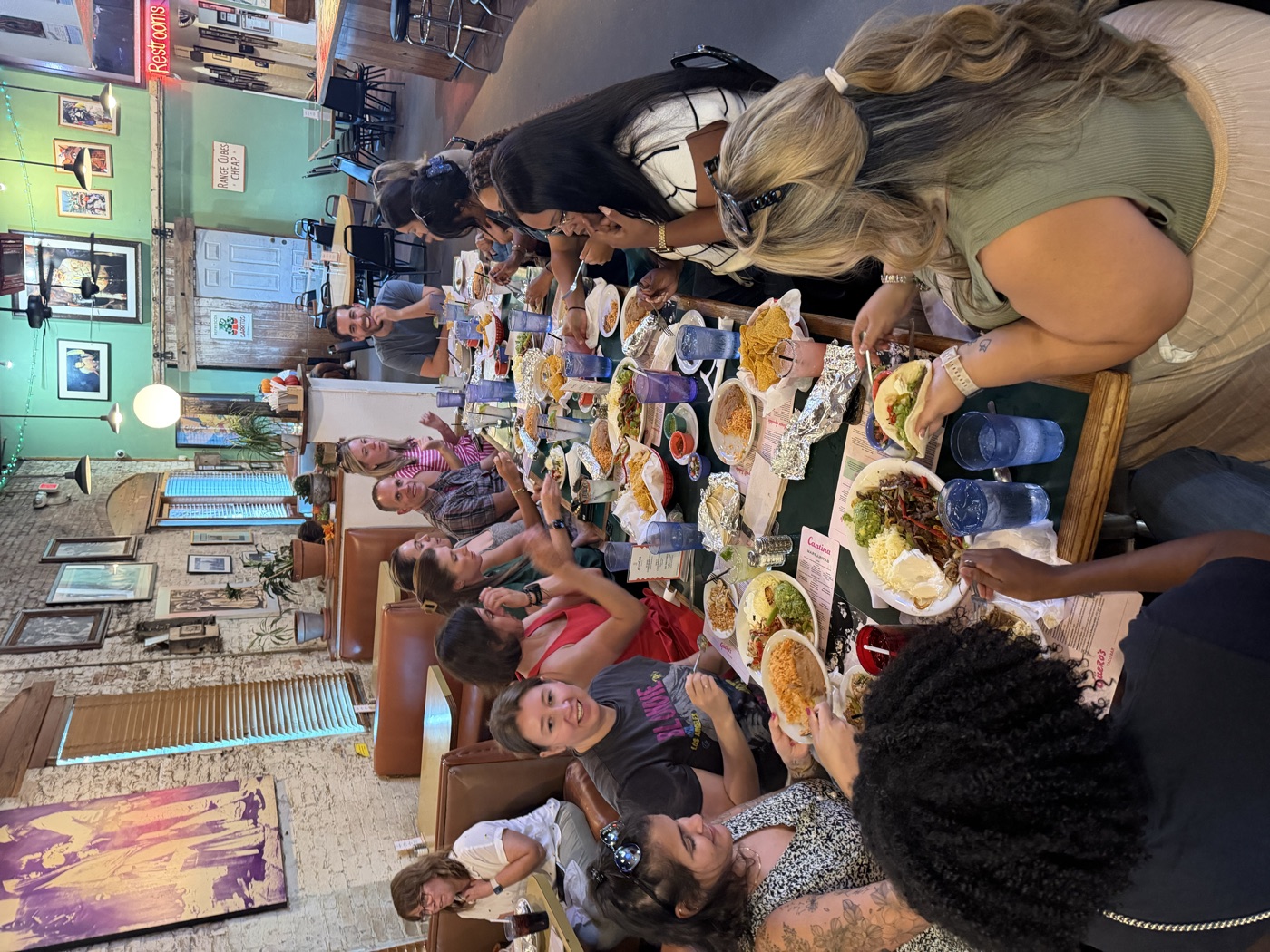 A large group sharing tacos and plates at one long restaurant table