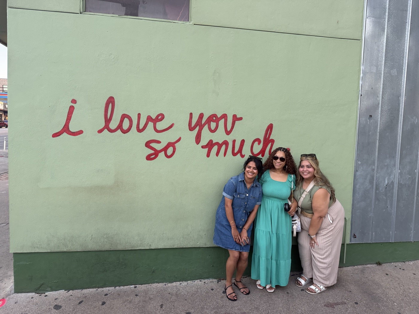 Three guests smiling in front of the “i love you so much” mural in Austin