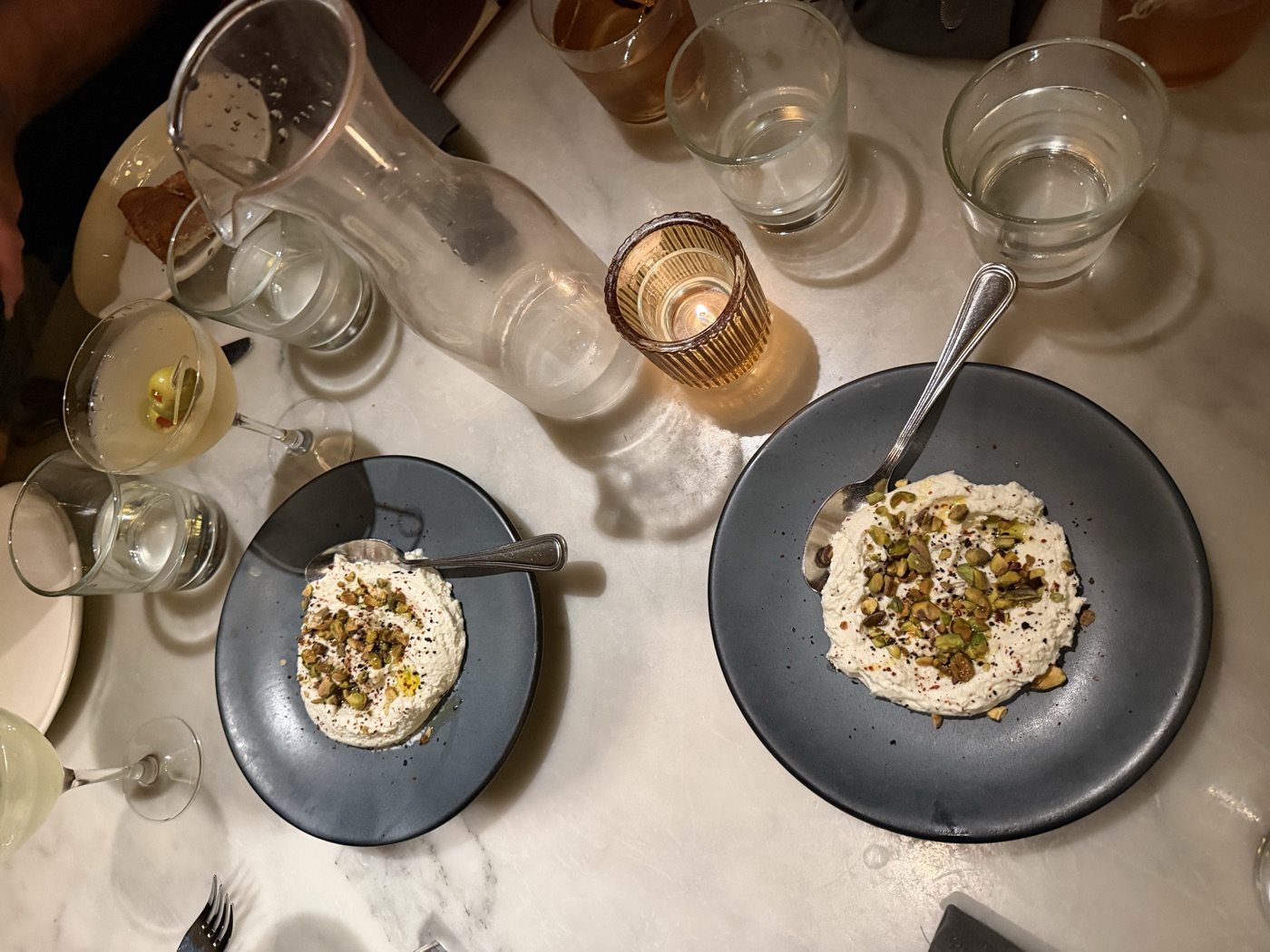 Two plates of whipped ricotta with pistachios and cocktails on a marble table